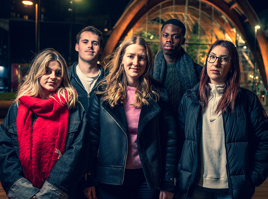 Five students standing together at night in front of a building.