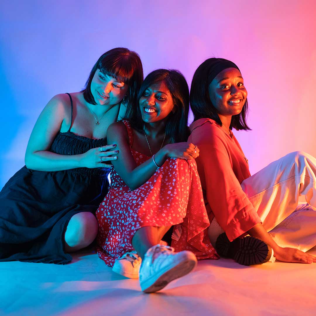 Three friends sat on the floor, huddled up and smiling.