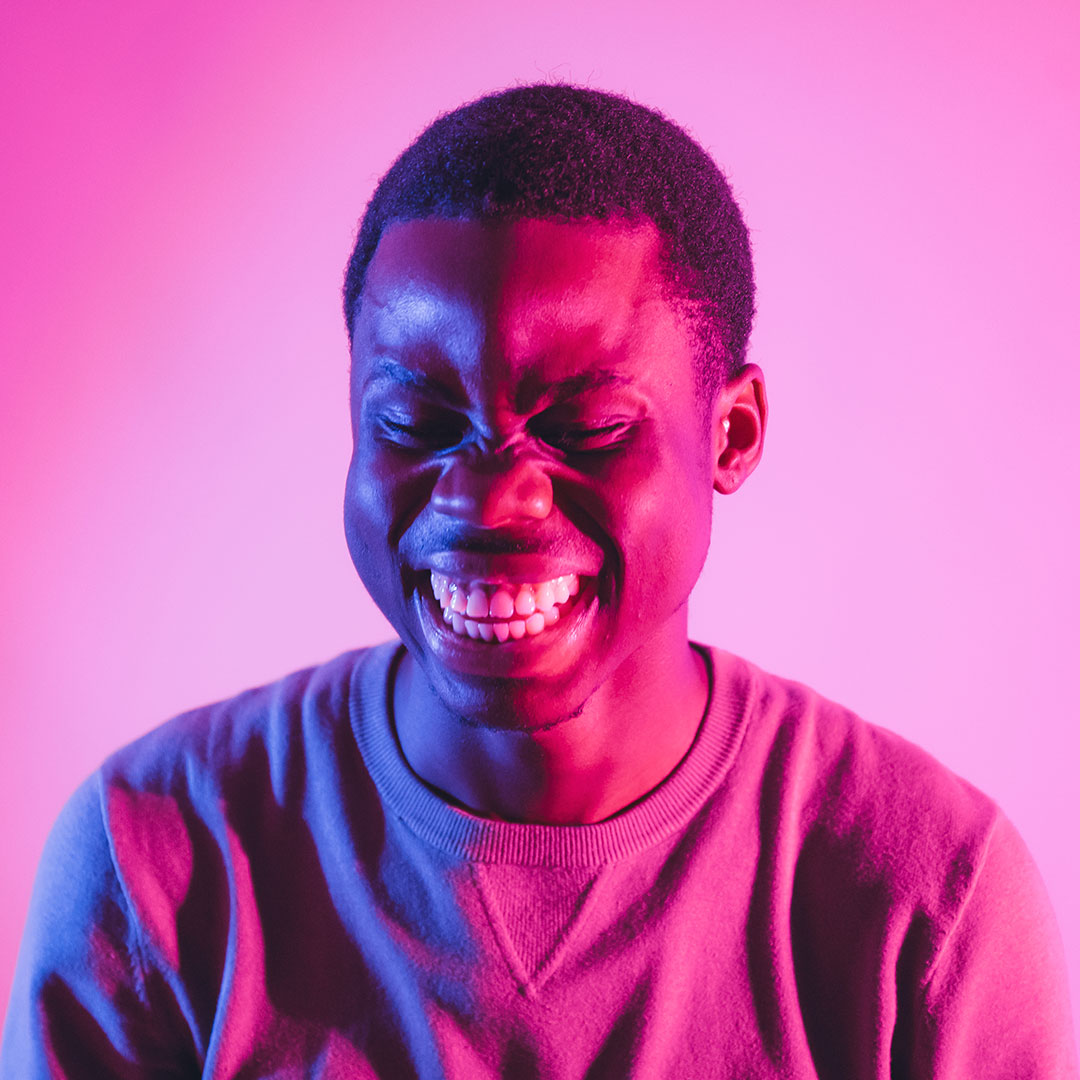 Student with eyes closed laughing and backlit with pink lights